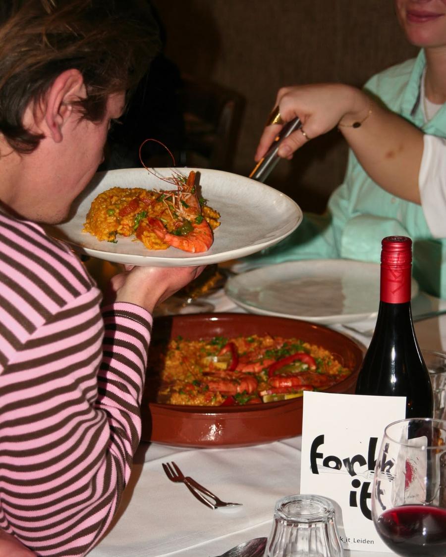 A Fork It paella plated with grilled prawns and a glass of wine