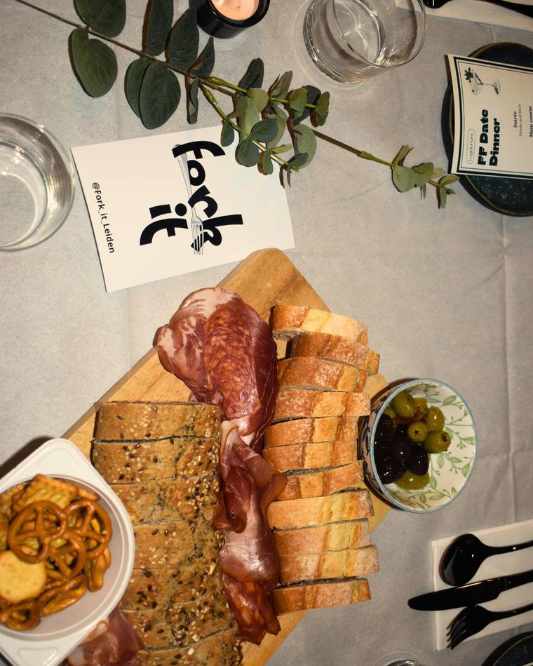 An overhead shot of a Fork It charcuterie board with a date dinner menu card