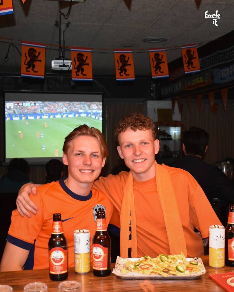 Two friends celebrating with beers and nachos during a football match
